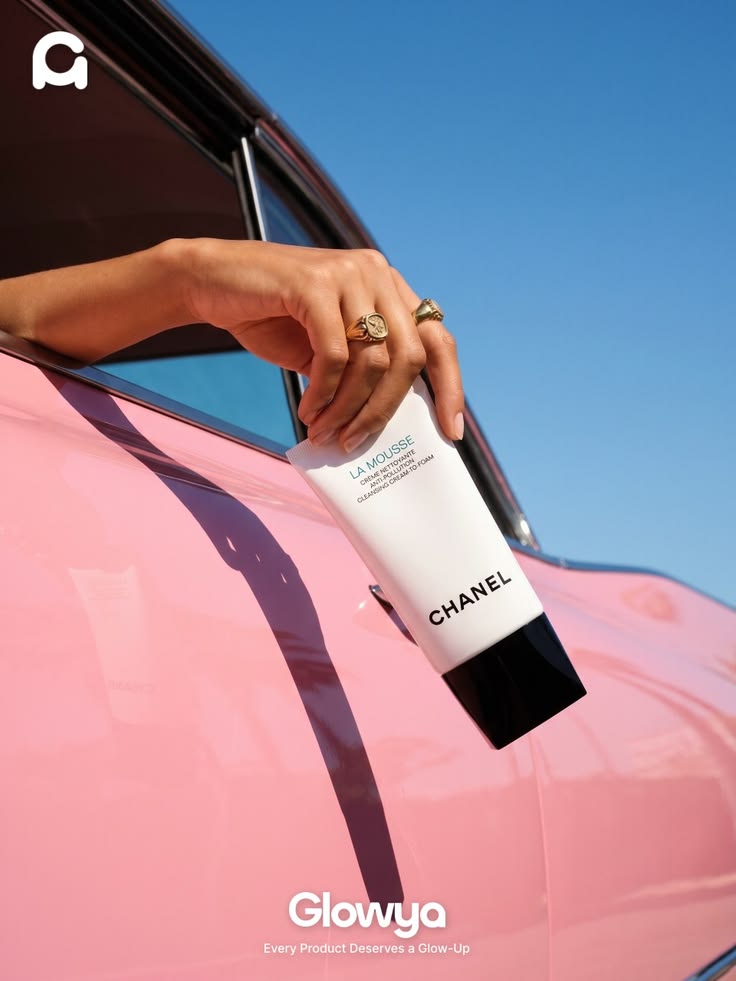Glowya post: a hand holding a cleansing cream tube out of the window of a pink car against a blue sky